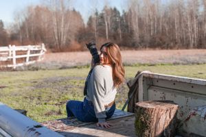 Photographer sitting in truck bed taking pictures with professional camera.