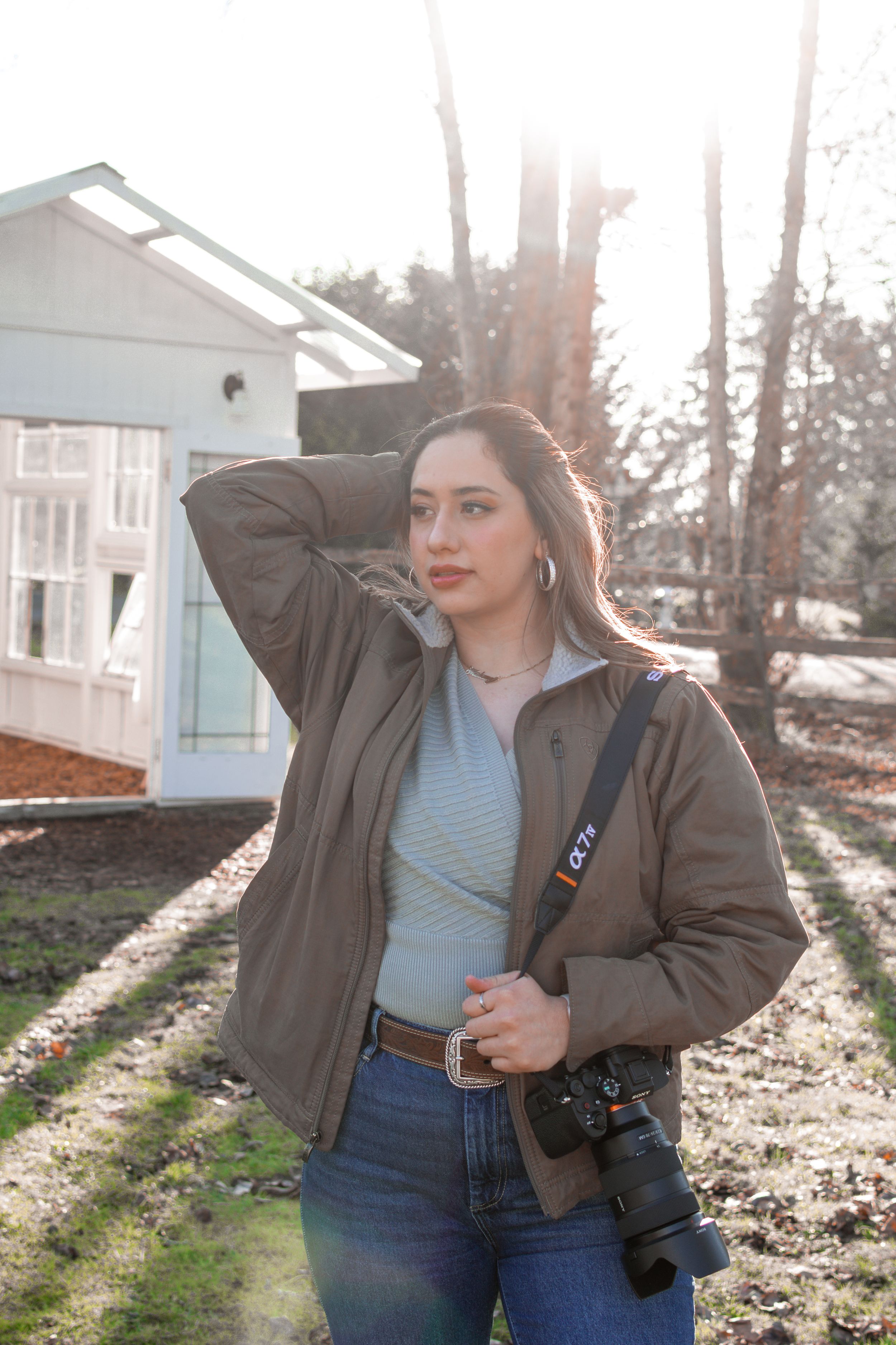 Photographer in brown jacket poses with professional camera equipment outdoors.