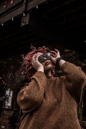 Person in brown sweater adjusting sunglasses against dark background.