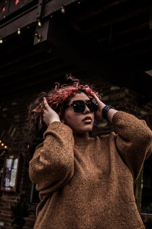 Person in brown sweater runs hands through hair outdoors.