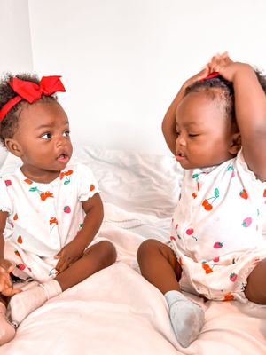 Two adorable babies in matching polka dot onesies sitting together on white bedding.