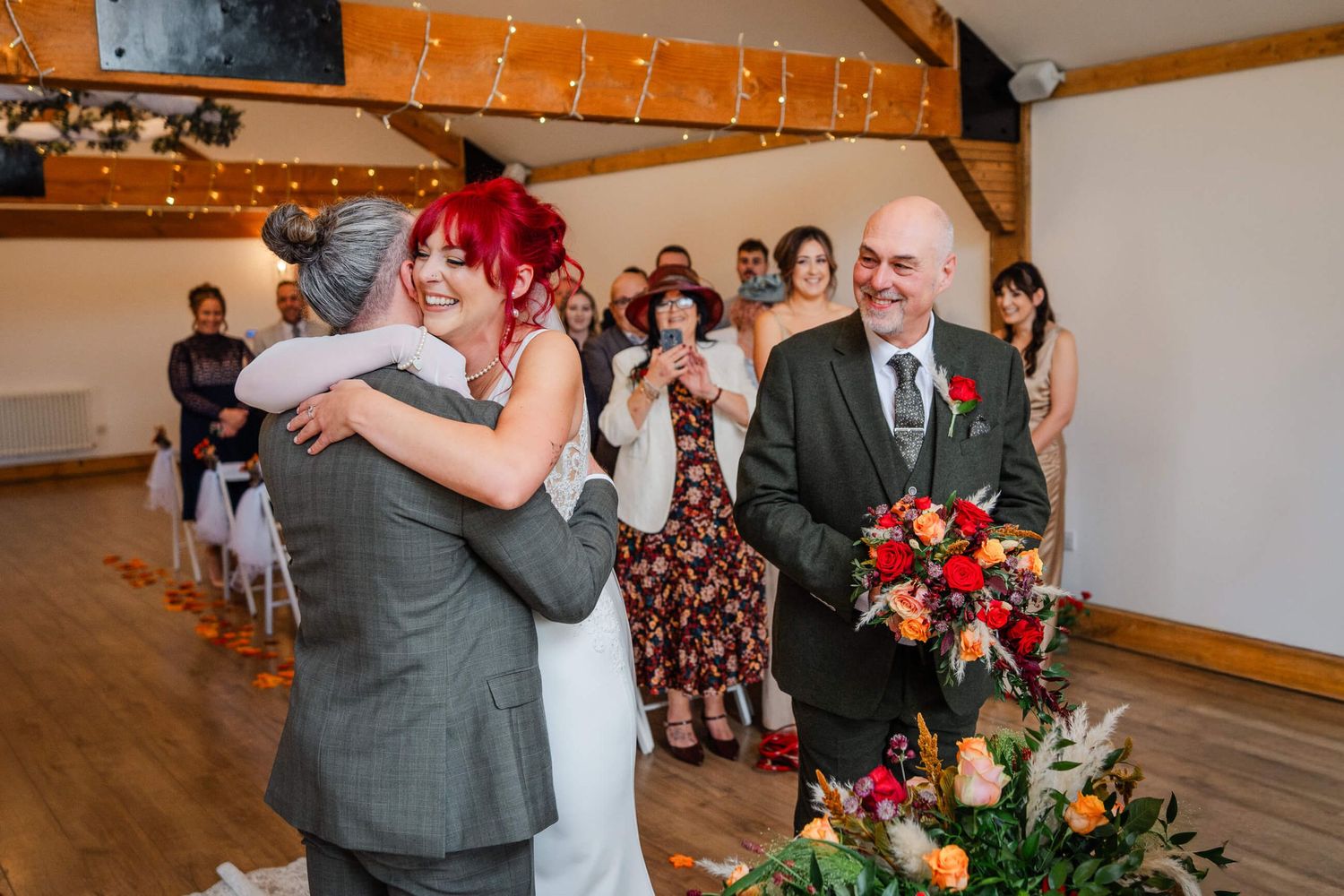 bride and groom hug at a Kent wedding with father of the bride holding wedding flowers