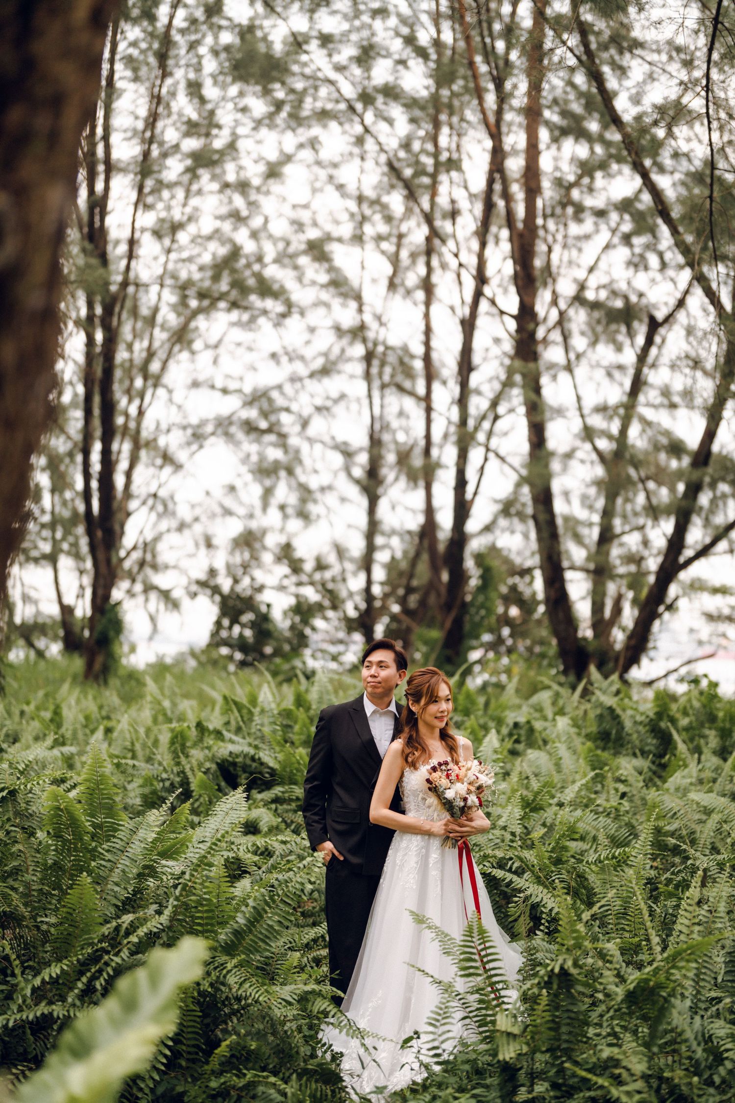 Wedding couple shares romantic moment among tall trees and wild ferns.