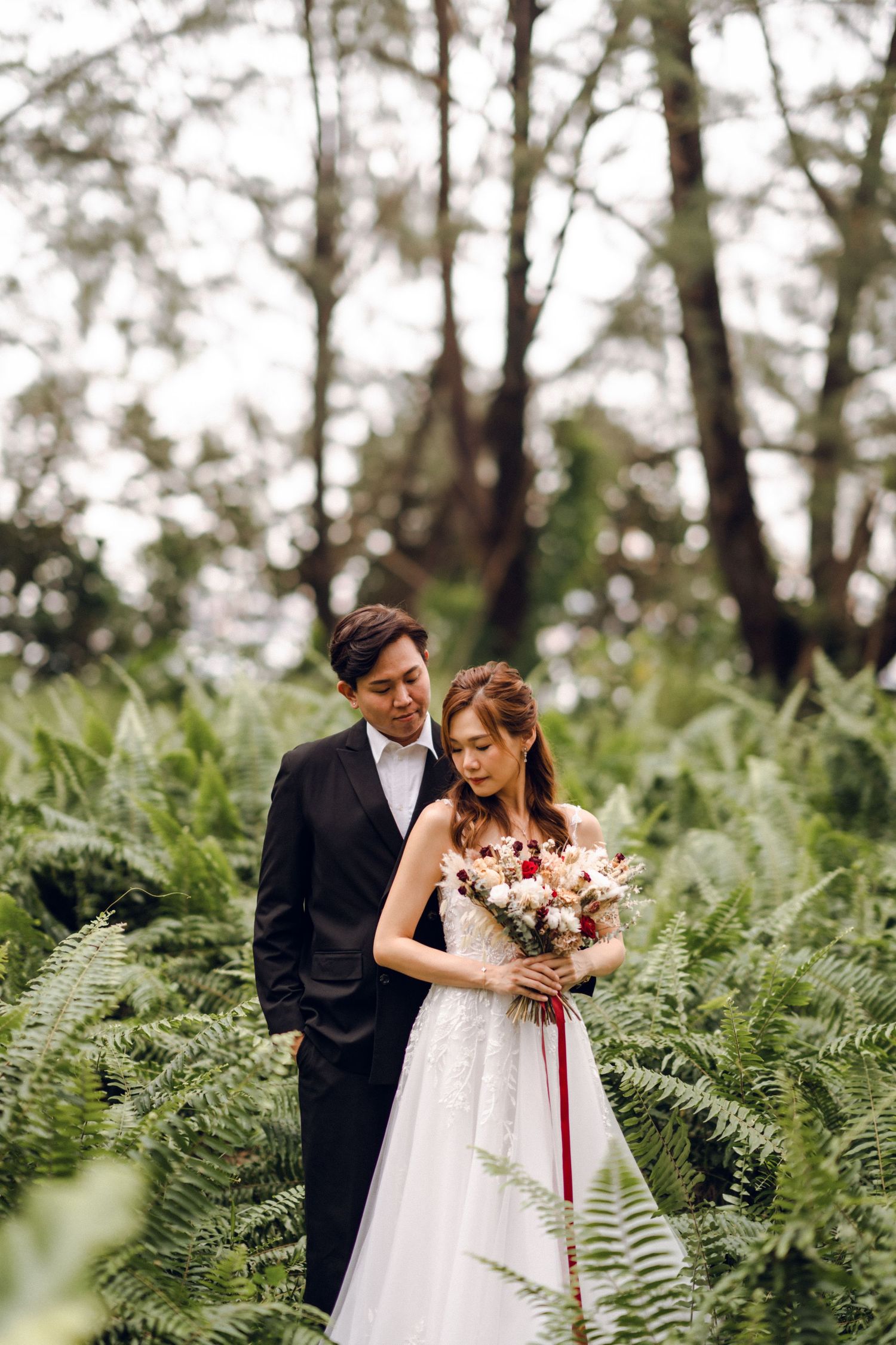 Newlyweds share intimate moment surrounded by lush green ferns and forest trees.