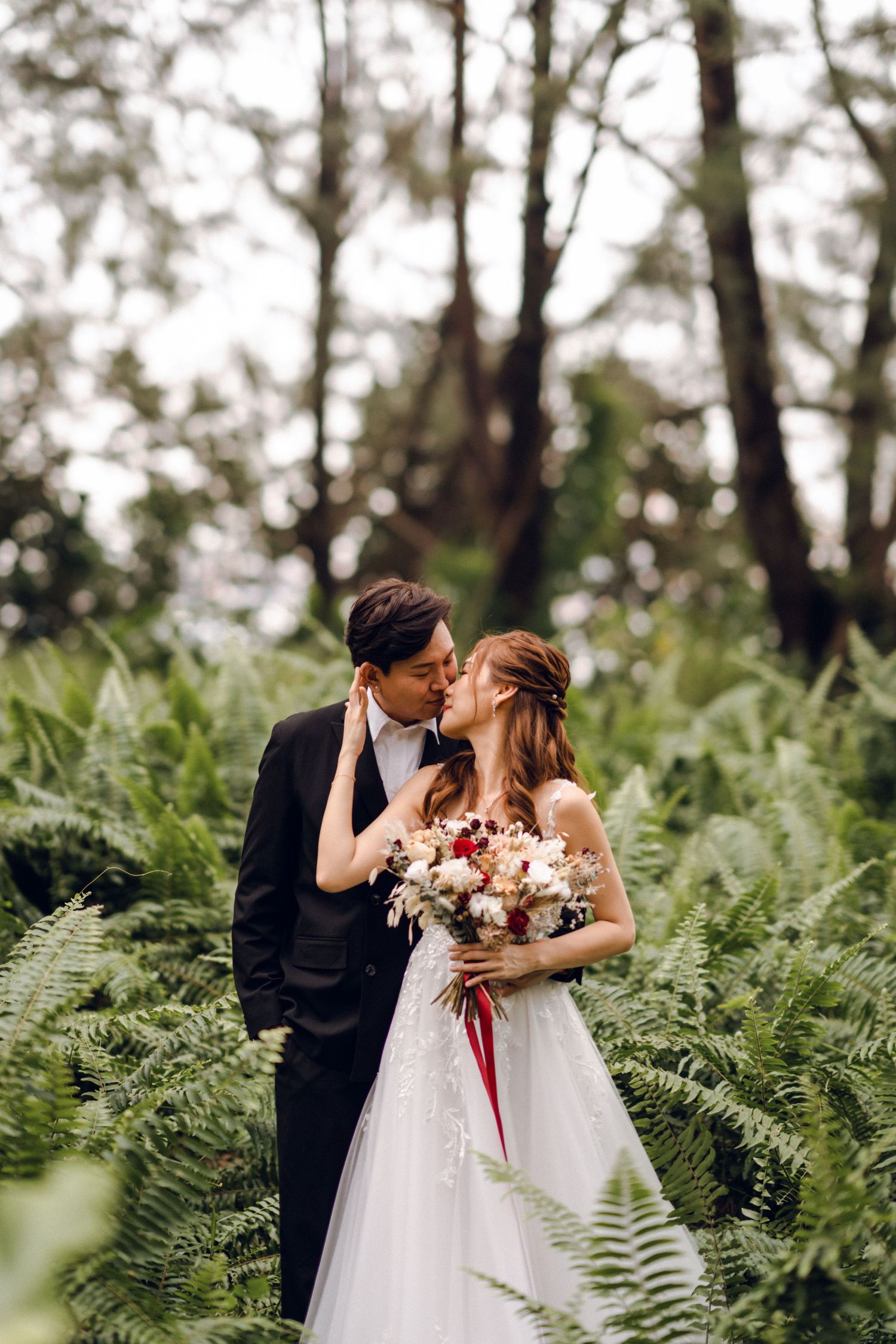 Romantic forest wedding photos with couple embracing among ferns.