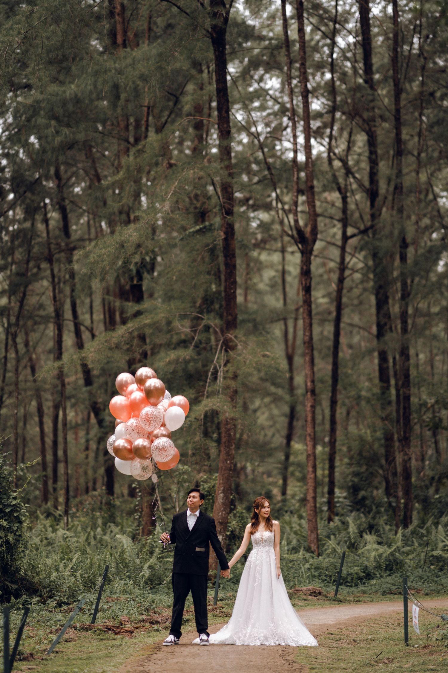 Elegant wedding portrait in forest with peach balloons adding whimsical touch.