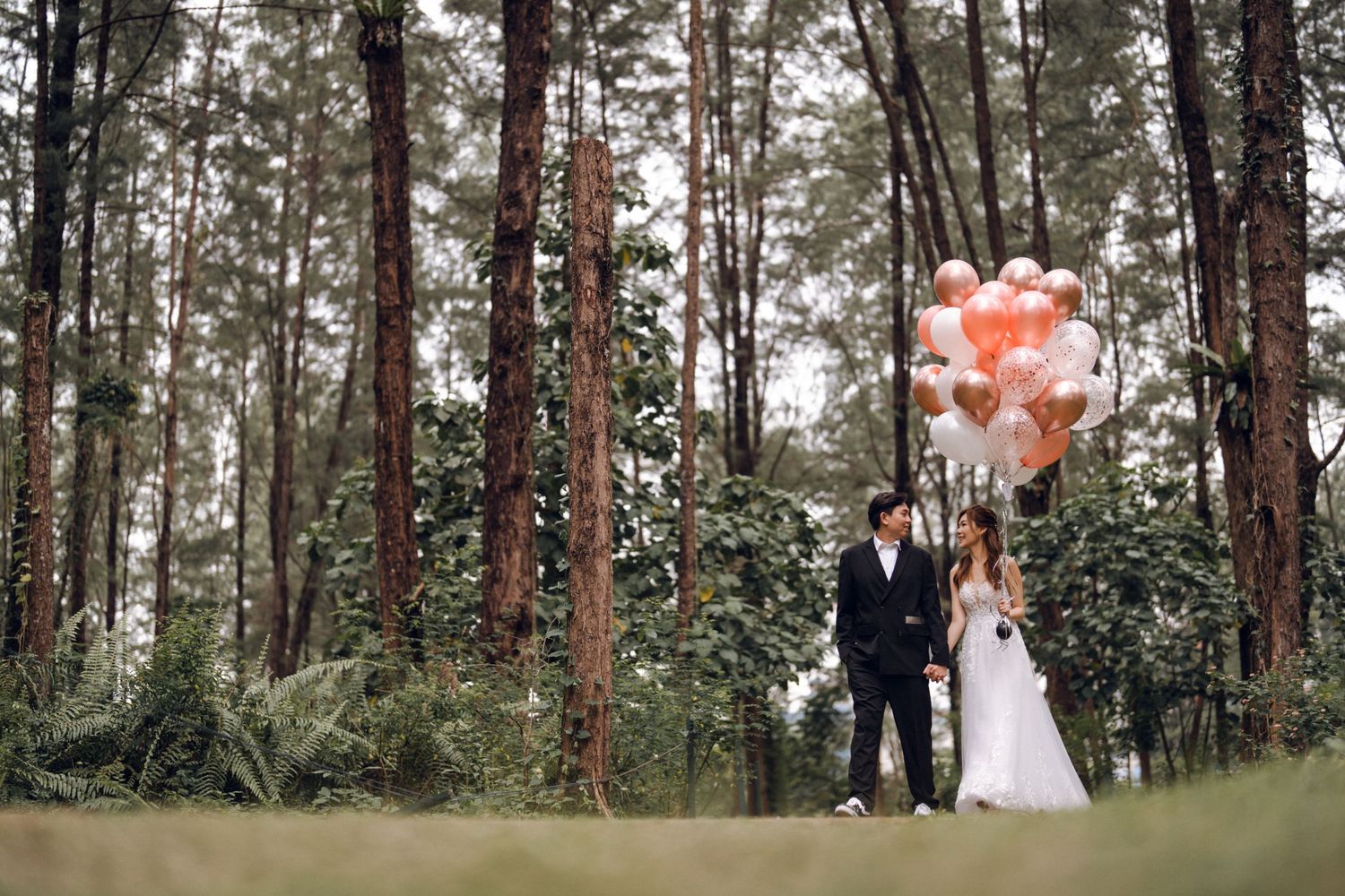 A romantic wedding photoshoot in a pine forest with peach and white balloons creating a dreamy atmosphere.