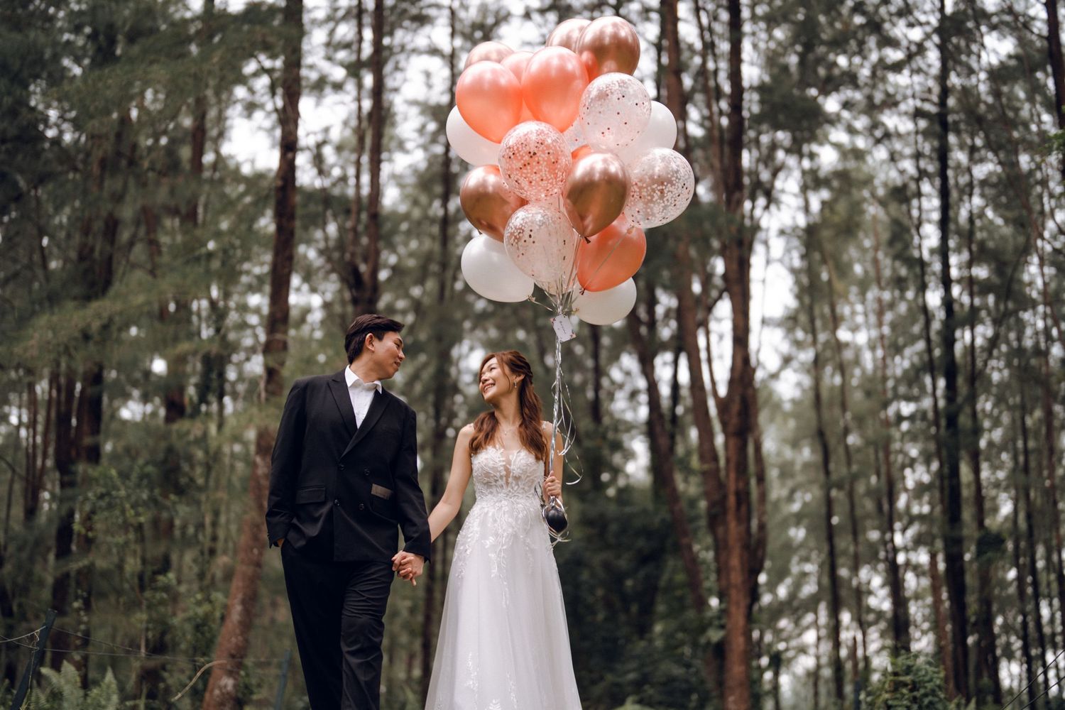 Newlyweds share intimate moments among tall pine trees with elegant balloon decorations.
