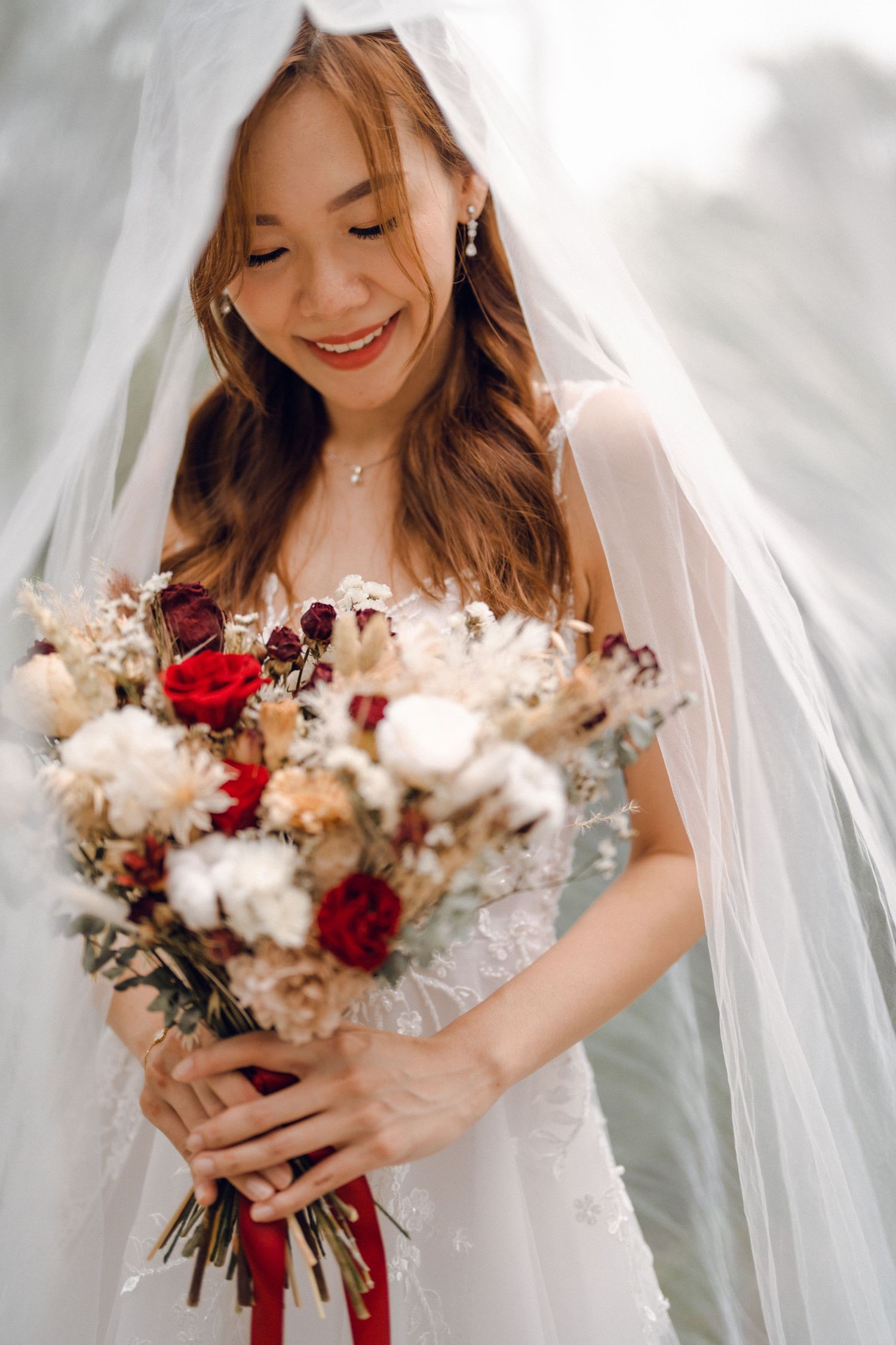 Beautiful bridal bouquet featuring red roses and dried flowers with delicate white veil details.