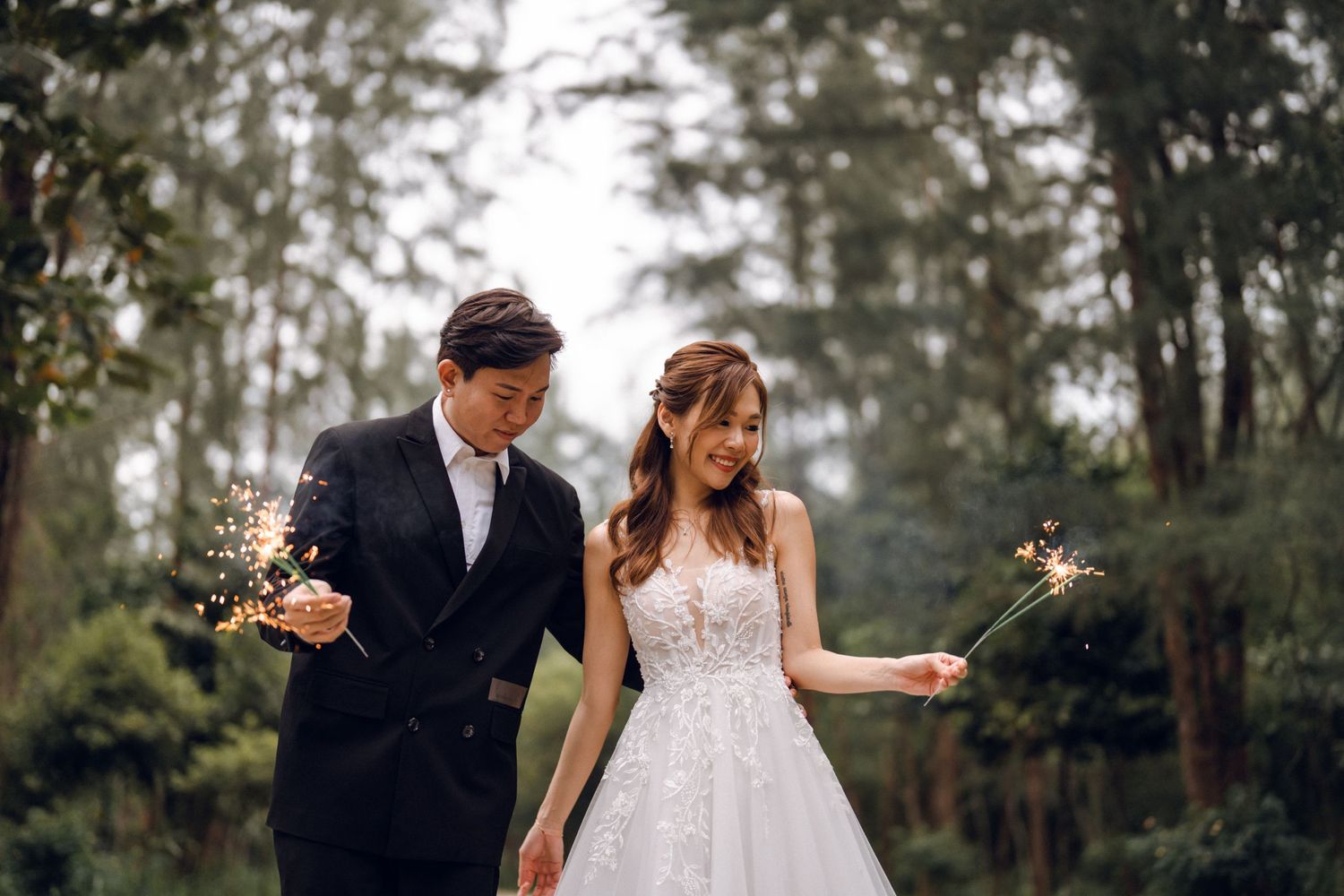 Couple holding sparklers during their forest wedding celebration.