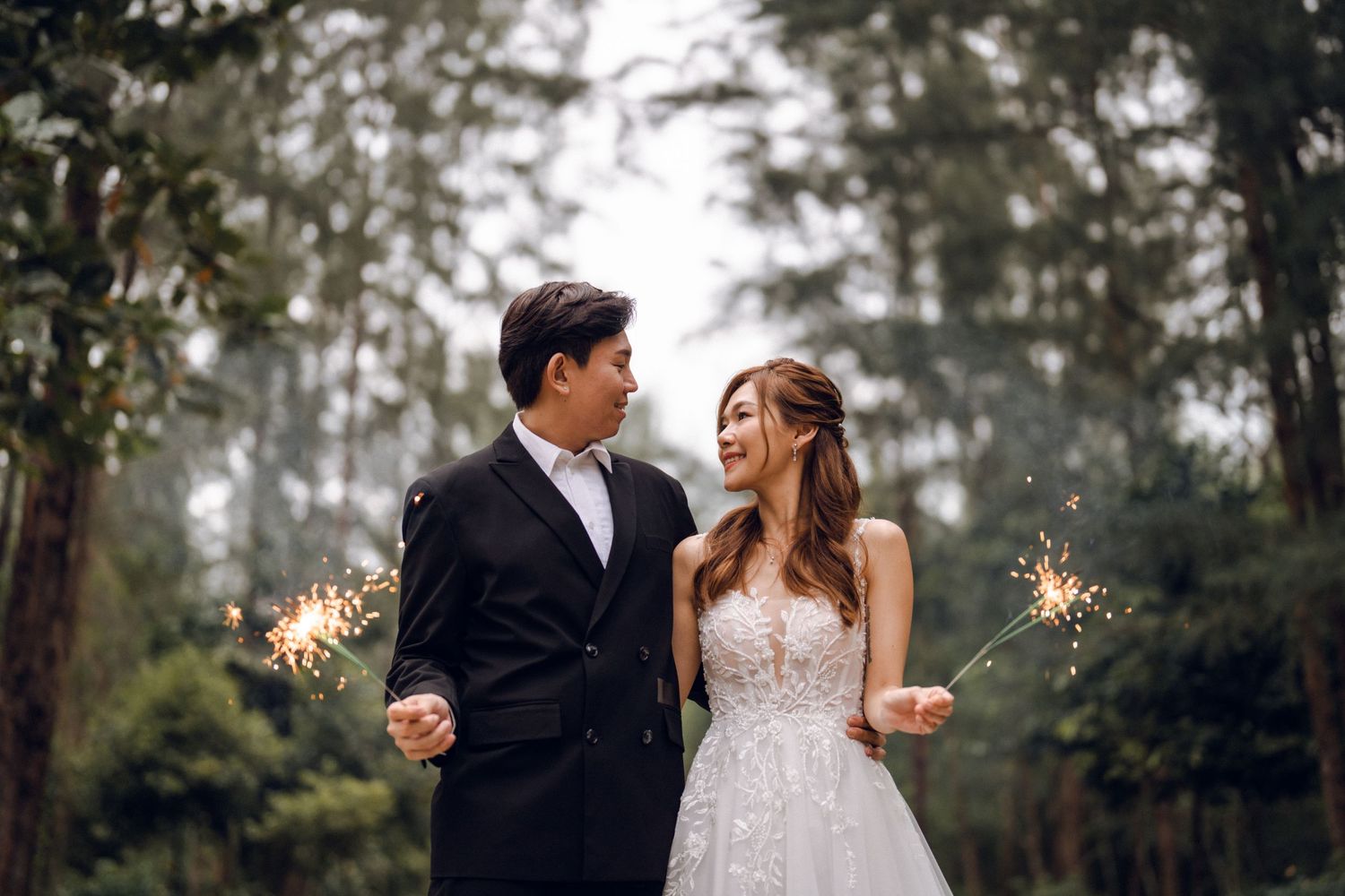 Romantic forest wedding scene with couple holding sparklers at dusk.