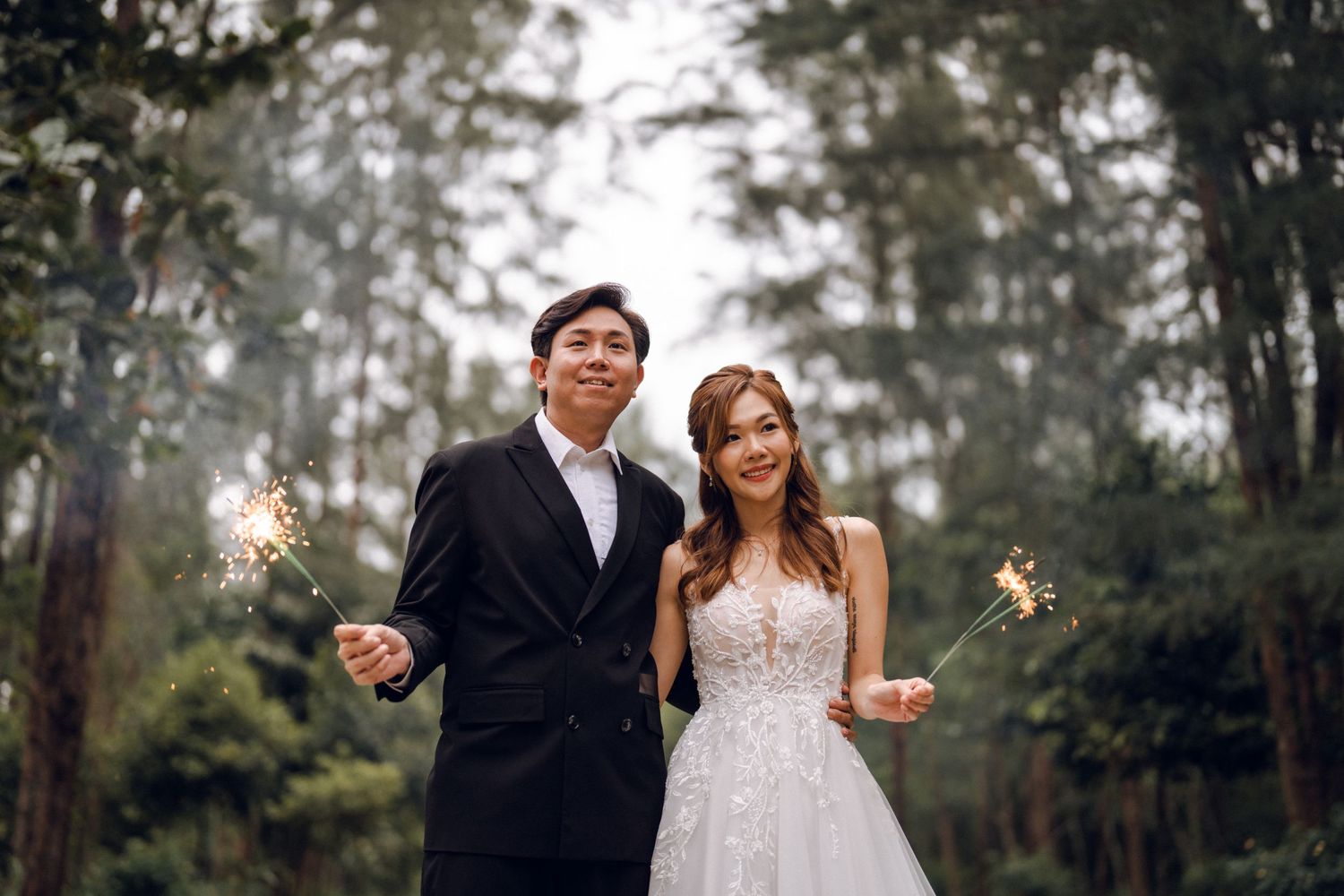 Wedding couple celebrating with sparklers in a magical forest setting.