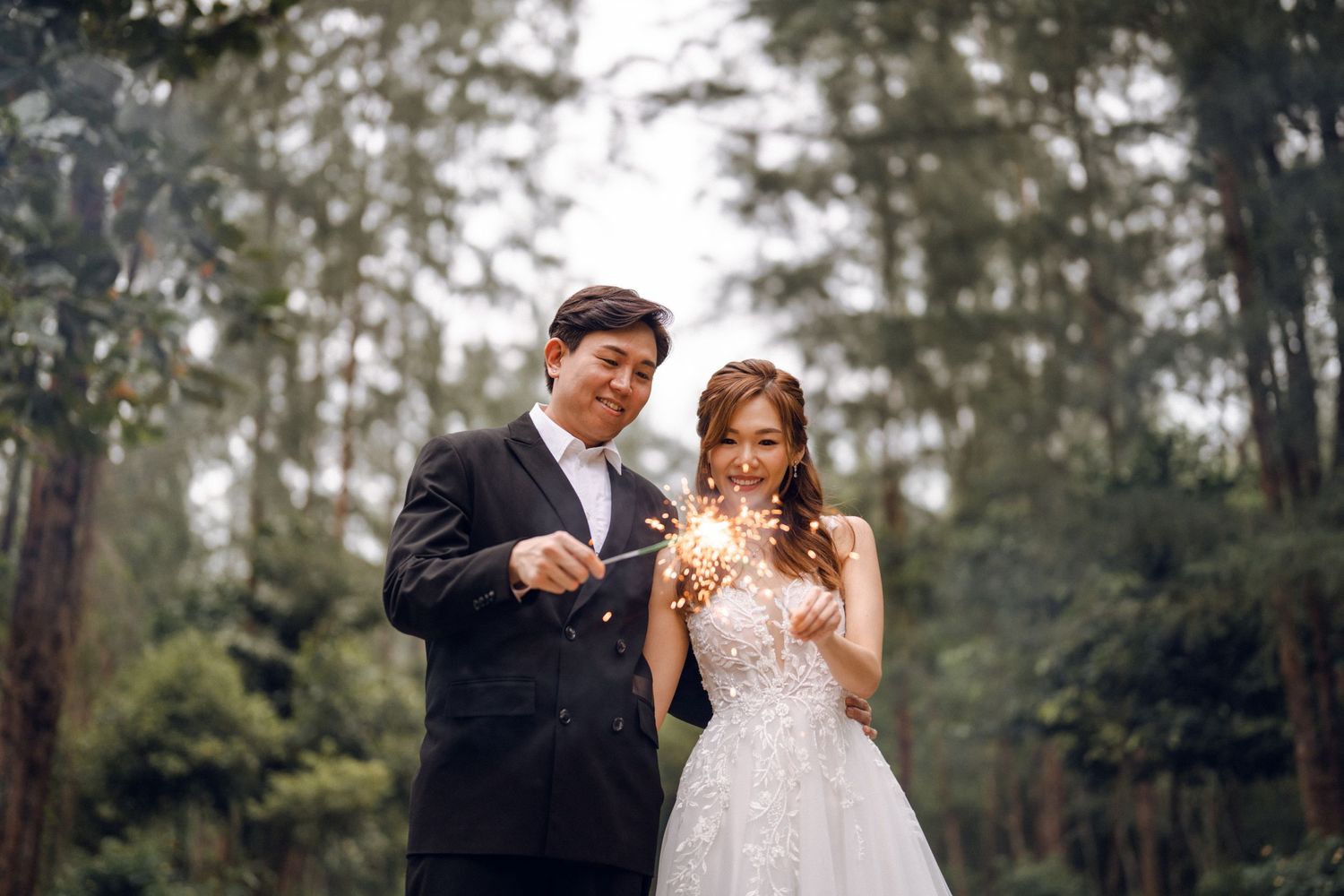Enchanting wedding moment captured with sparklers in a pine forest.