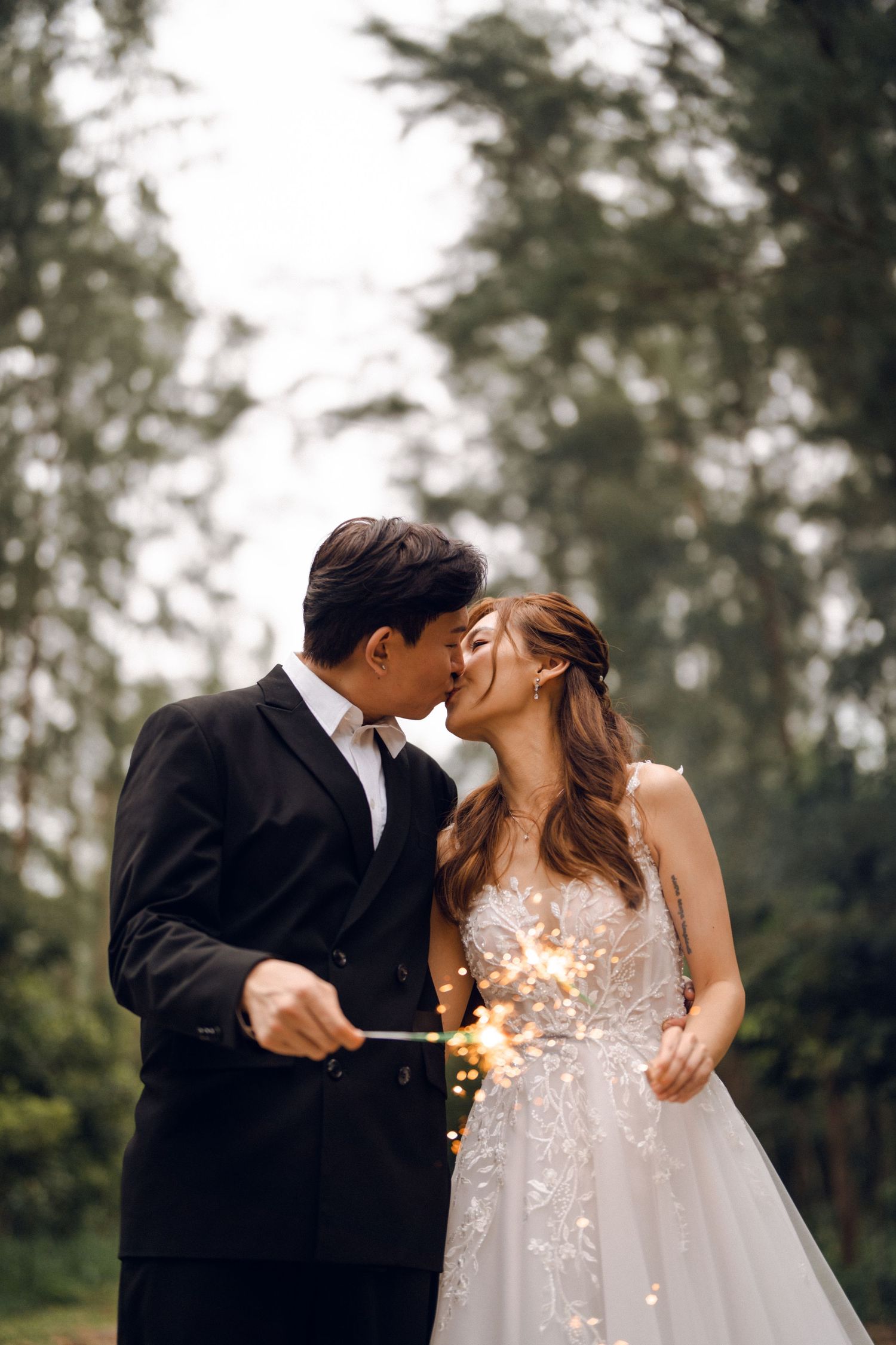 Romantic wedding kiss captured with sparklers in a forest setting.