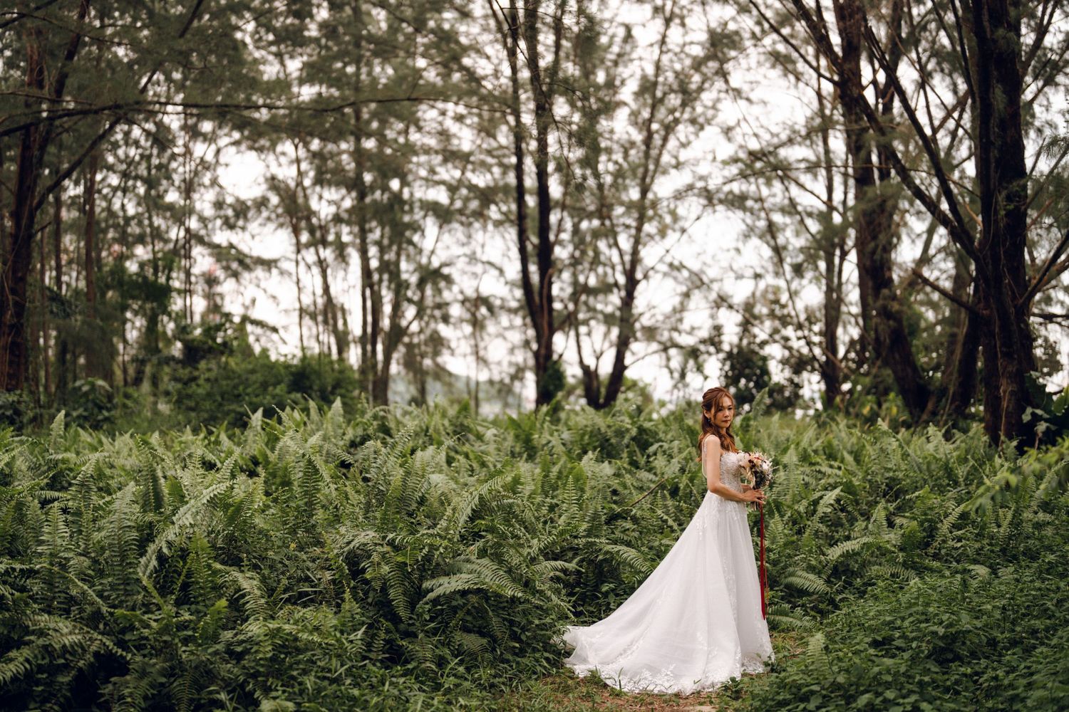 Wedding portrait amidst tropical greenery and tall trees.