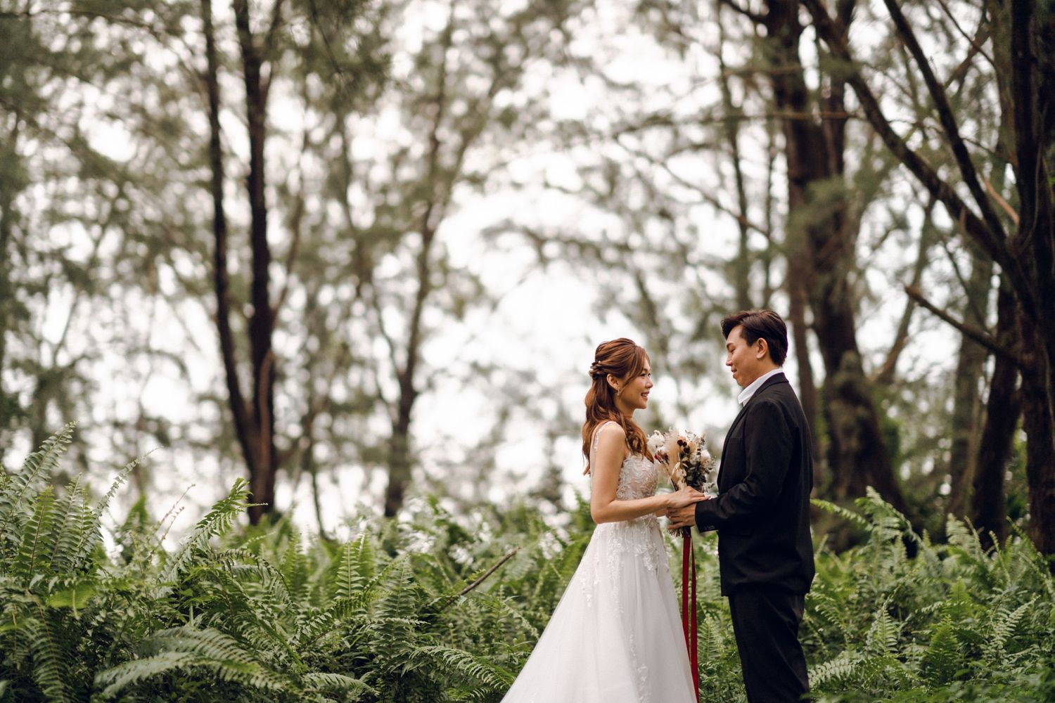 Romantic wedding moment captured in a serene forest setting with ferns.