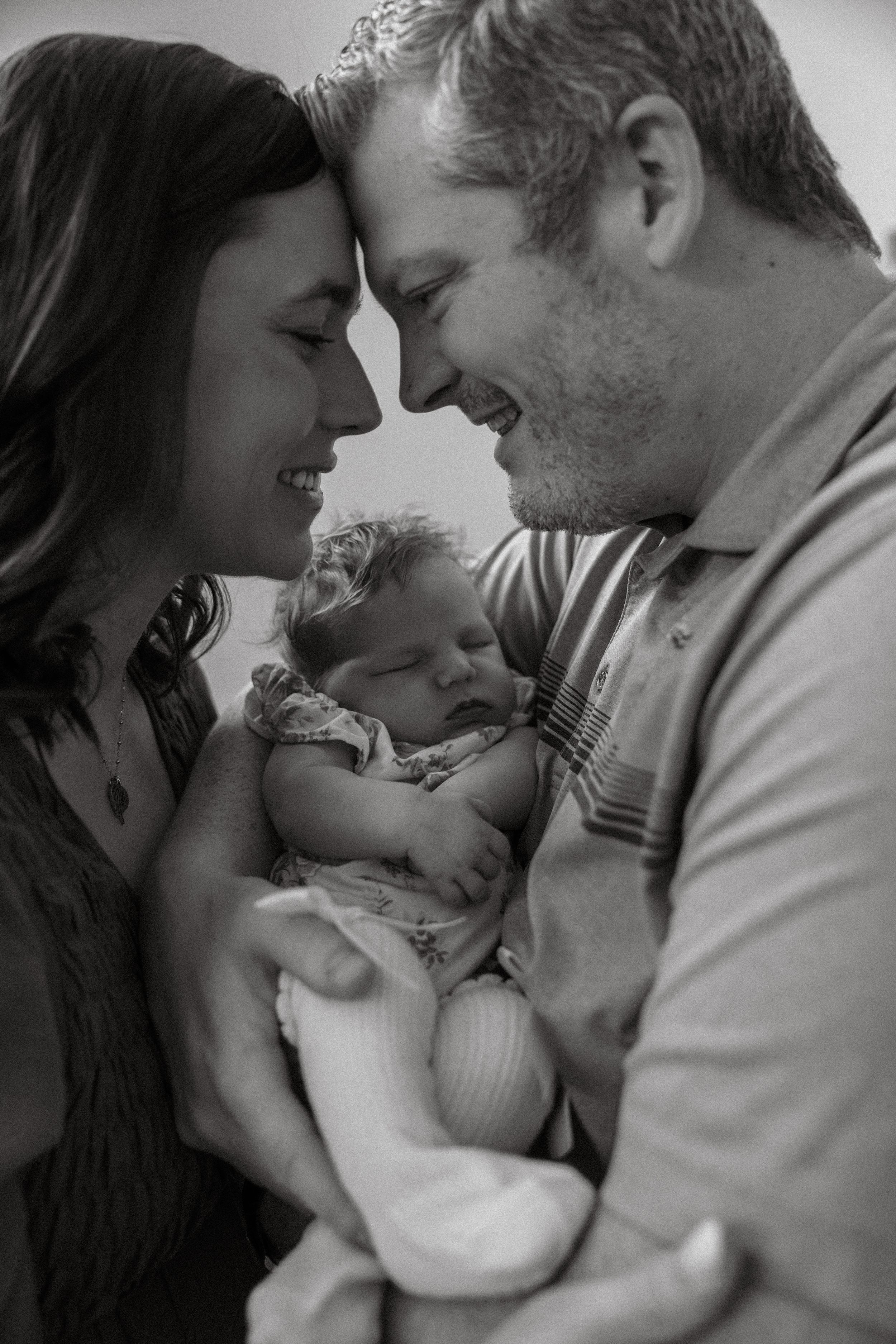 Black and white intimate photo series capturing tender family moments with parents gazing lovingly at their baby.
