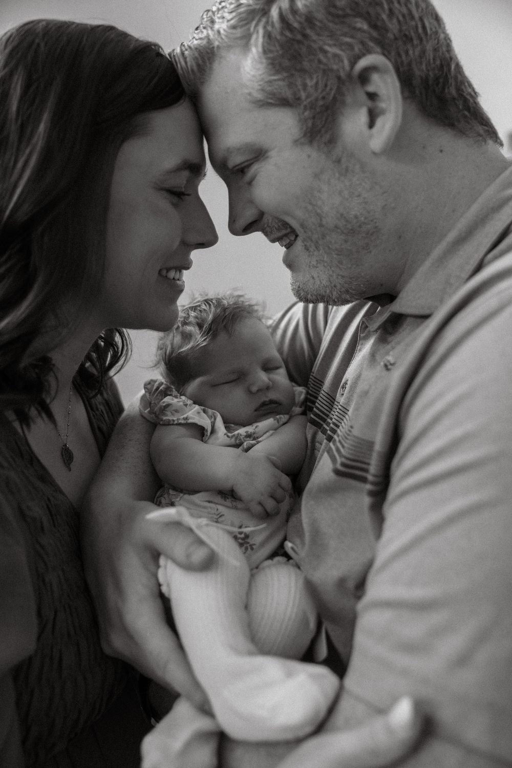 Black and white intimate photo series capturing tender family moments with parents gazing lovingly at their baby.