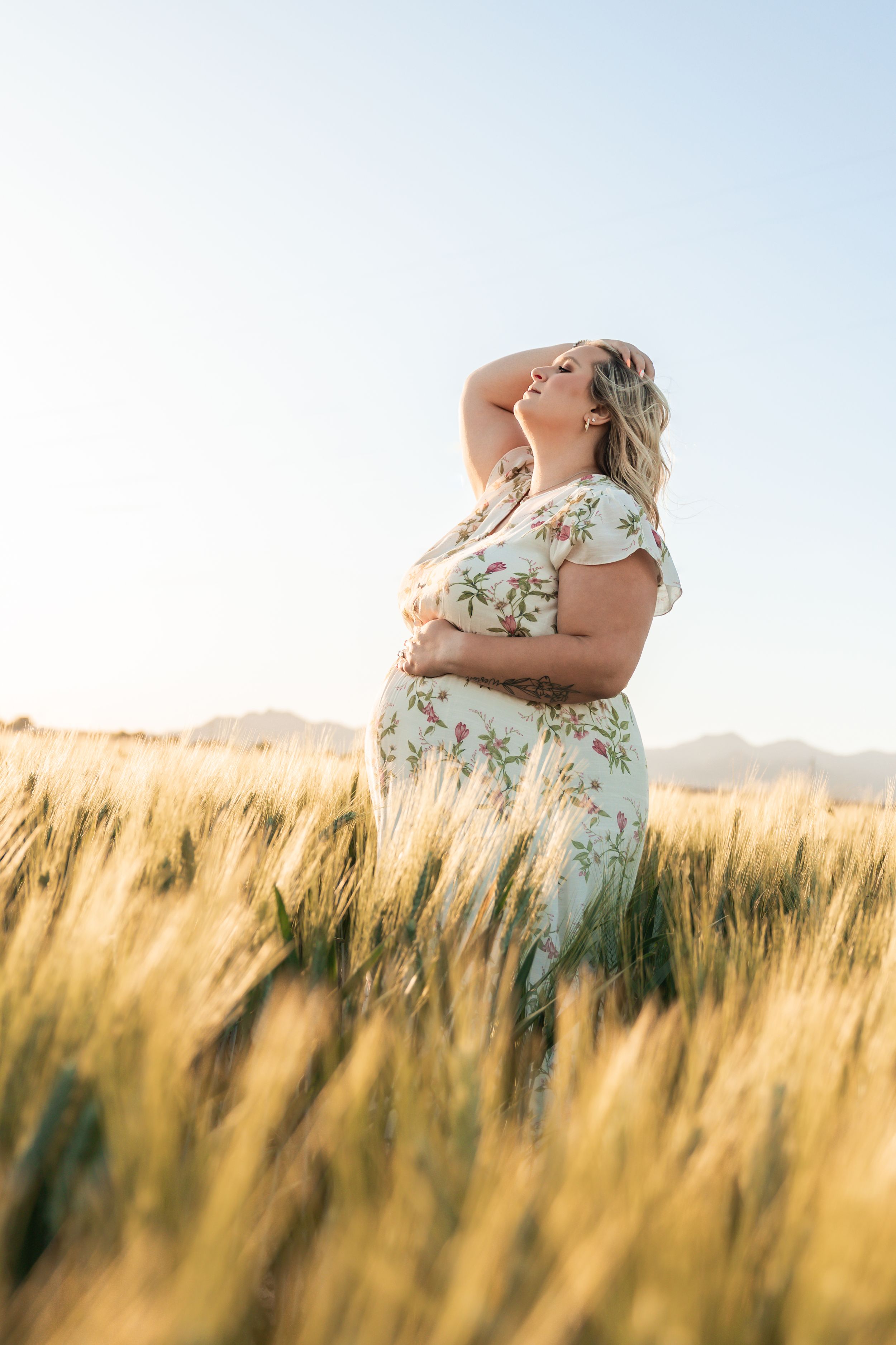 A floral dress stands out against a golden wheat field at sunset, creating a dreamy summer scene.