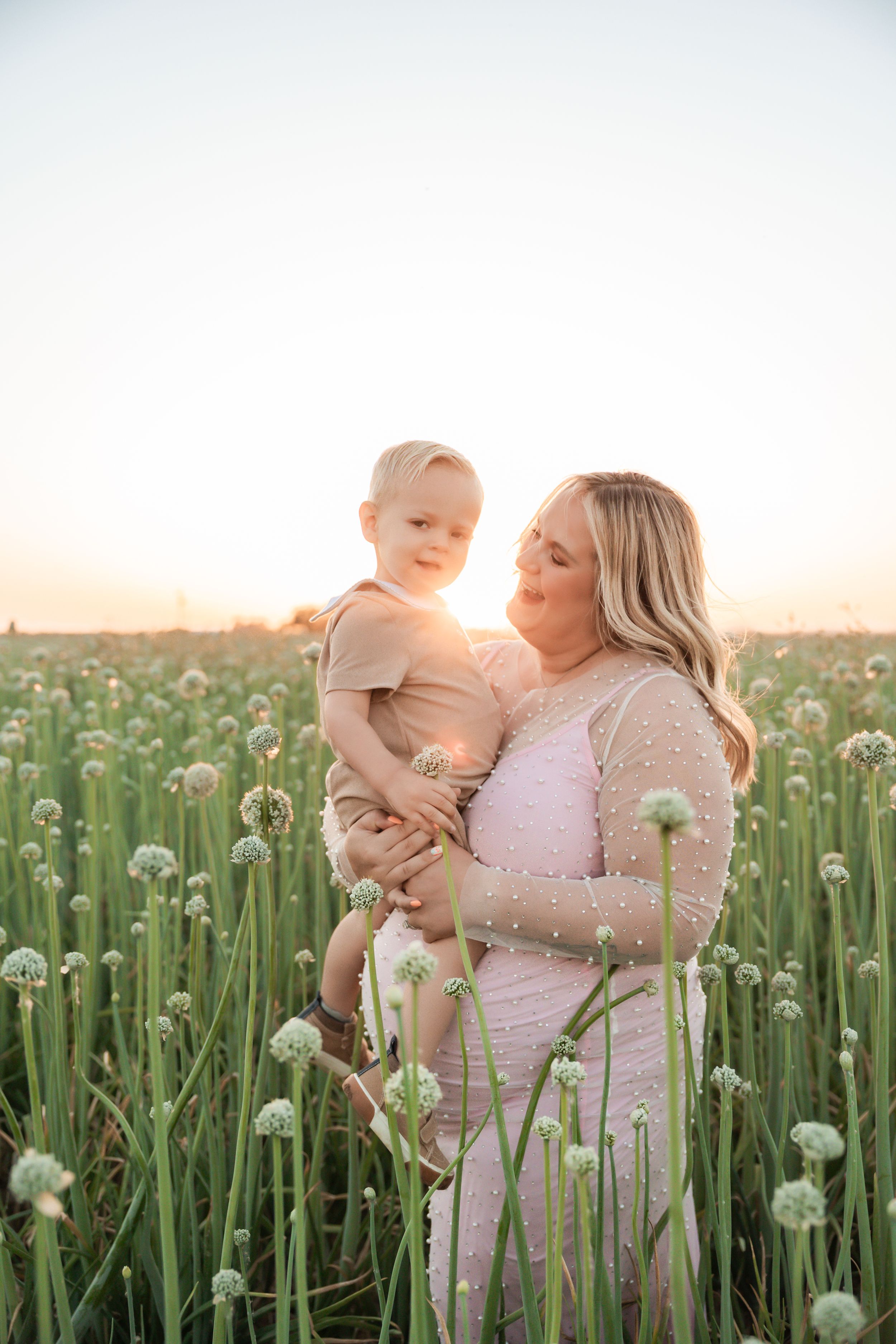 Parent and child share tender moments together in a field of blooming white dandelions at sunset.
