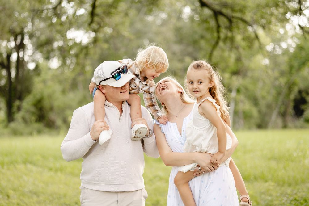 Happy family with two young children enjoying a sunny day outdoors in a lush green park, smiling and laughing together.