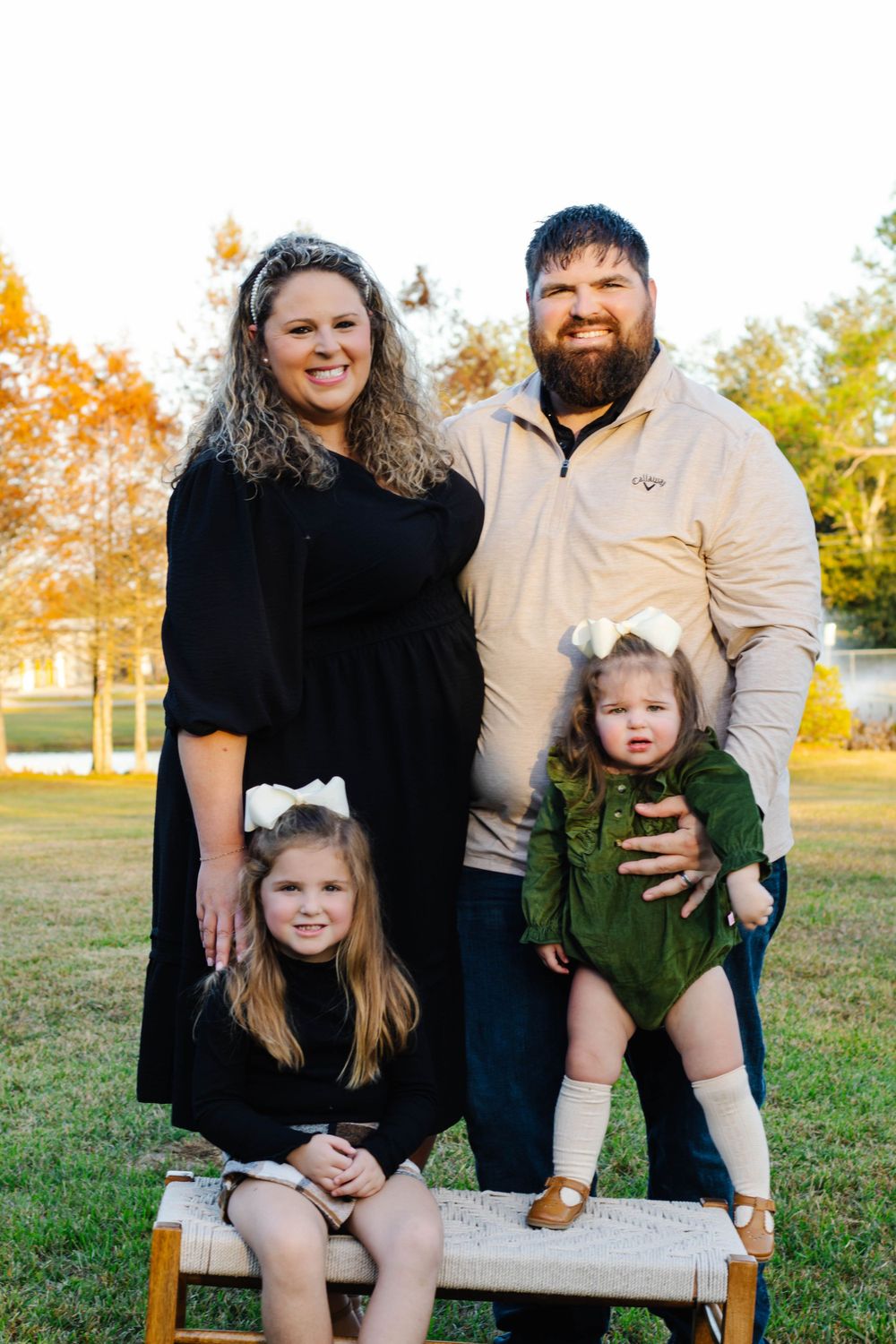 Family of four poses for outdoor portrait on wooden bench during golden hour in autumn.