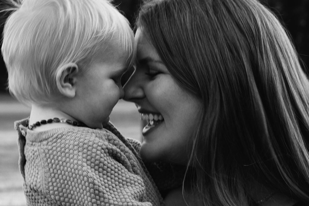 A tender black and white moment of a parent and young child touching noses while smiling.