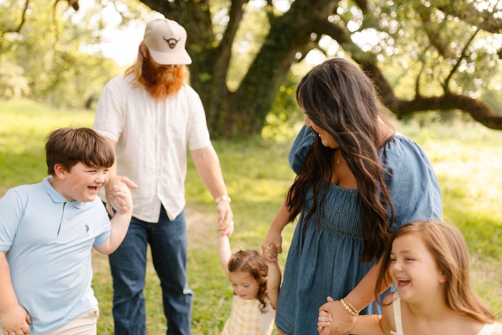 A joyful family of five laughing together outdoors in a lush green park during a sunny day.