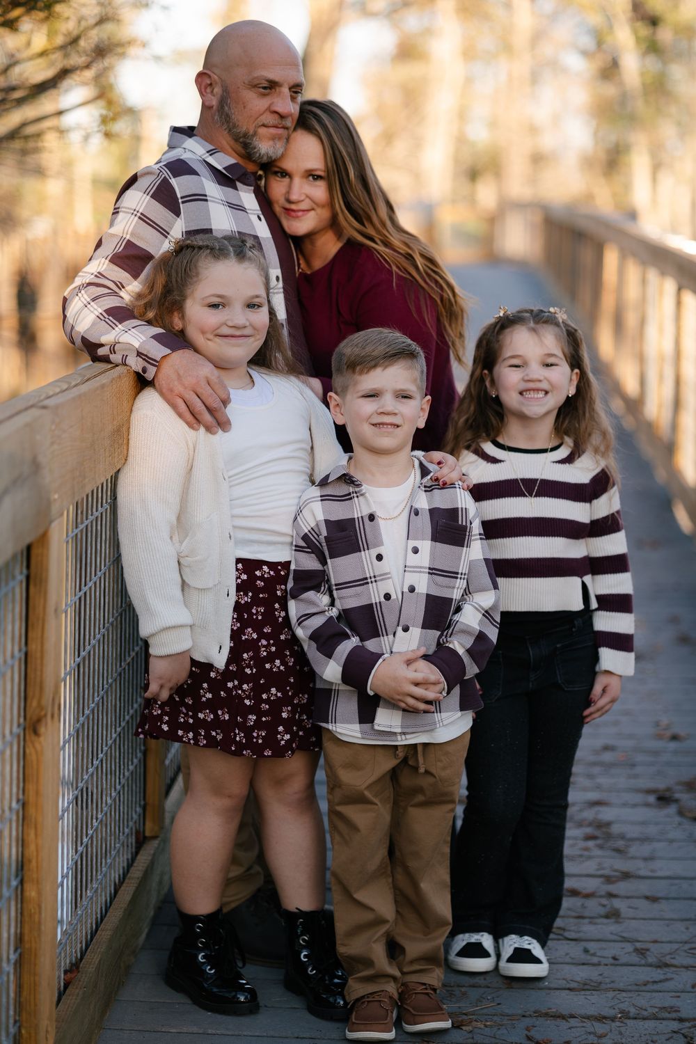 Family of five posing on a wooden bridge, parents behind three young children, dressed in coordinating fall outfits.