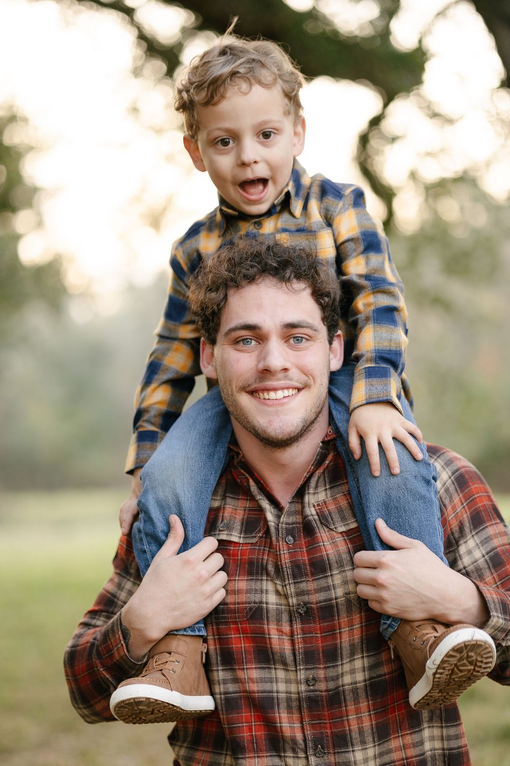 A father and young child play together outdoors in casual plaid shirts during golden hour.