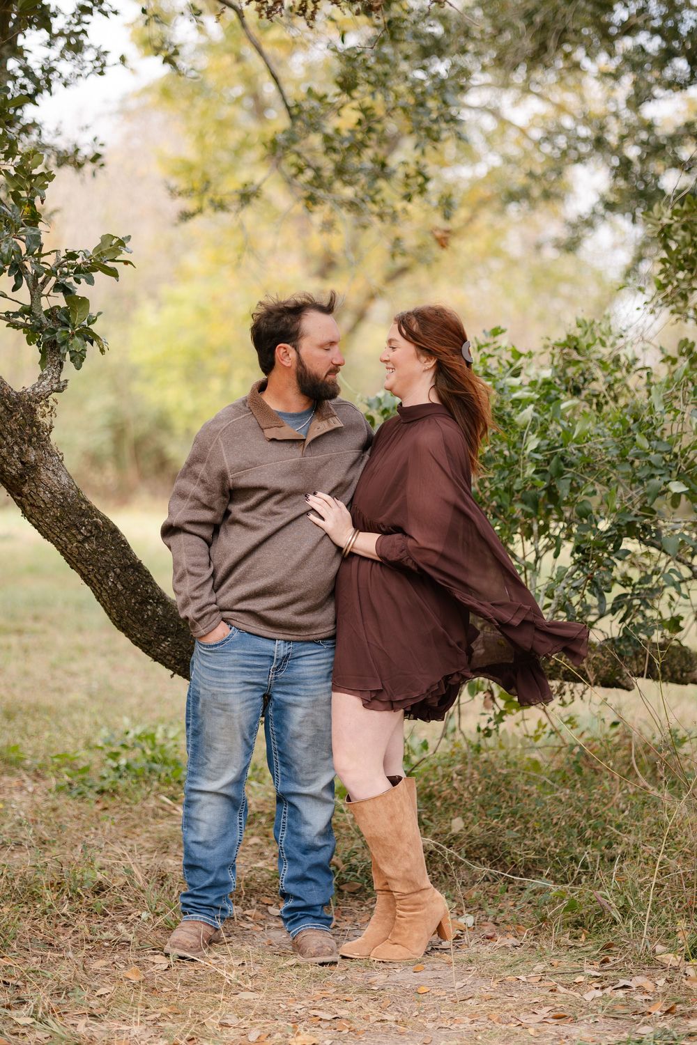 A couple in casual attire shares an intimate moment under a tree branch in an outdoor autumn setting.
