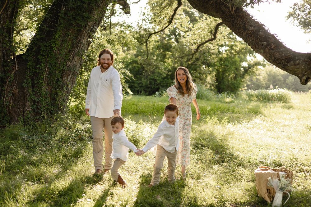 A family plays and walks together through a scenic outdoor setting with trees.