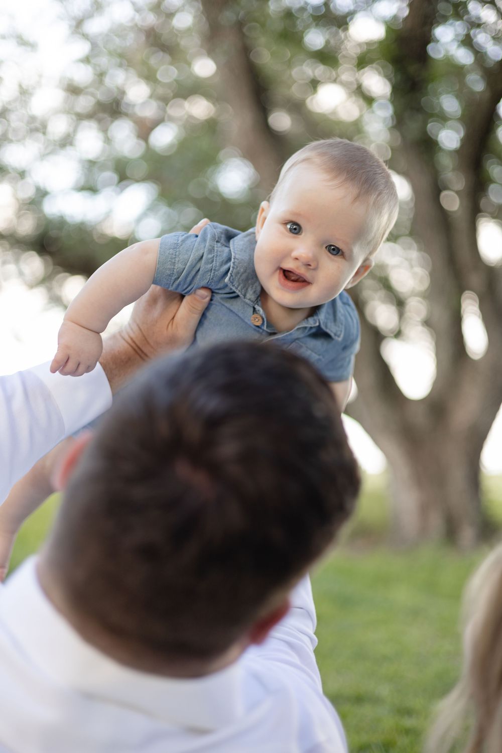 A joyful baby in blue clothing shares playful interactions during an outdoor photoshoot.
