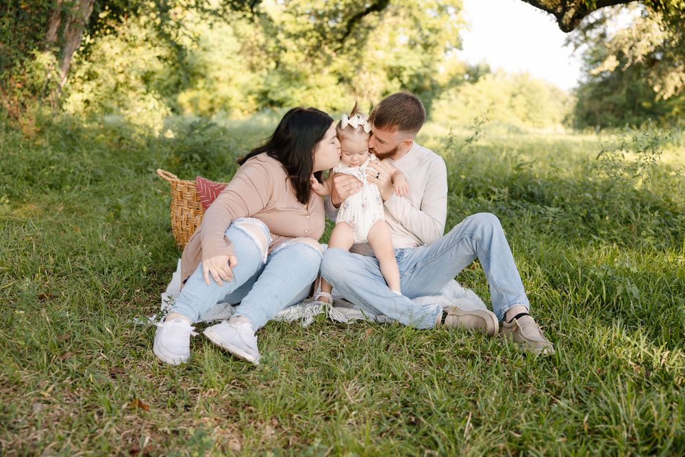 A couple relaxes together on a grassy hillside during a sunny outdoor photoshoot.