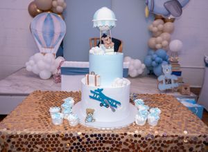 Blue and white tiered baby shower cake with hot air balloon theme and cloud decorations.