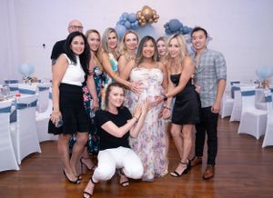 Group photo at a baby shower celebration with blue and white decorative balloon arch in the background.