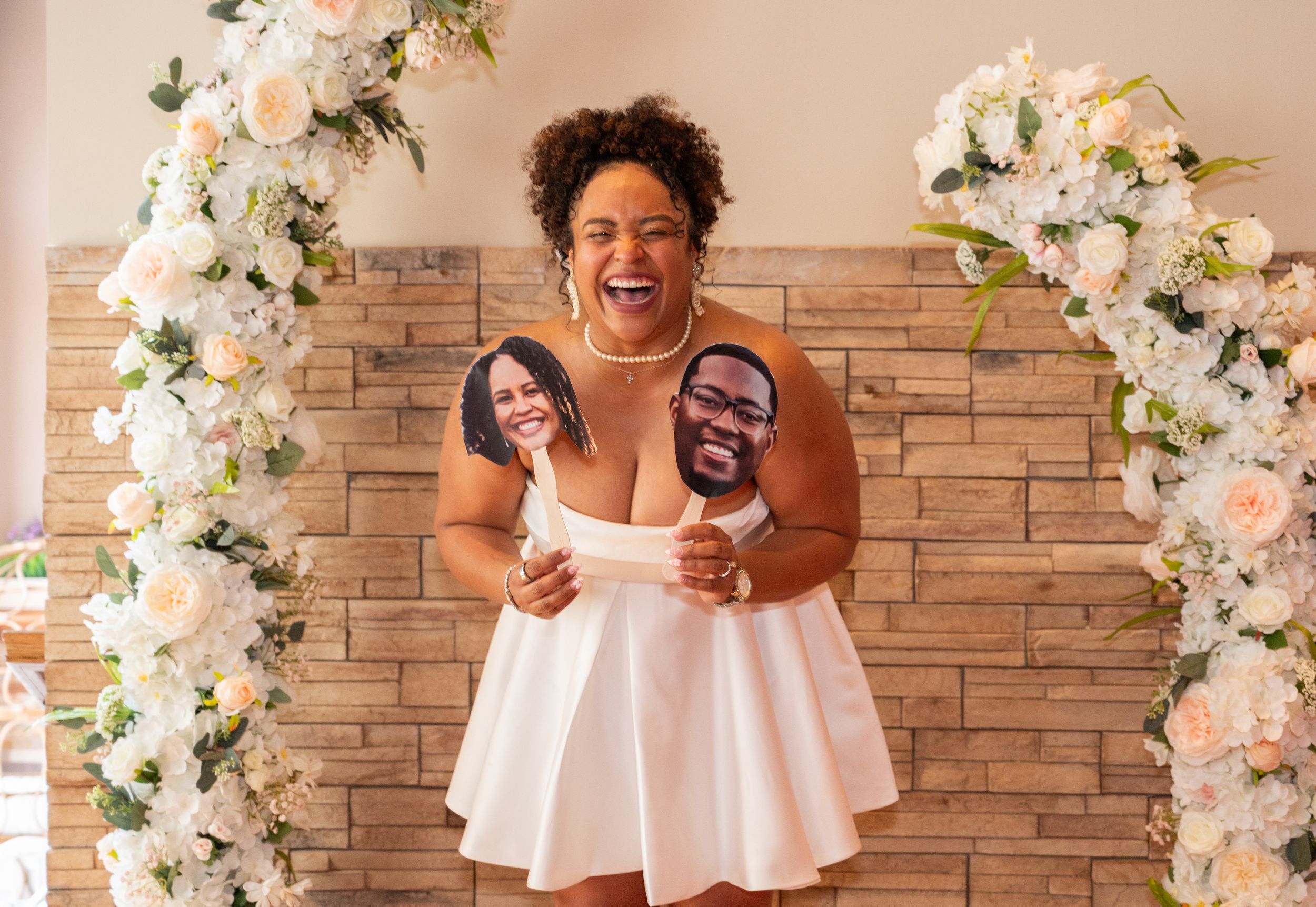 Celebratory poses in front of white floral arch decorations with natural lighting.