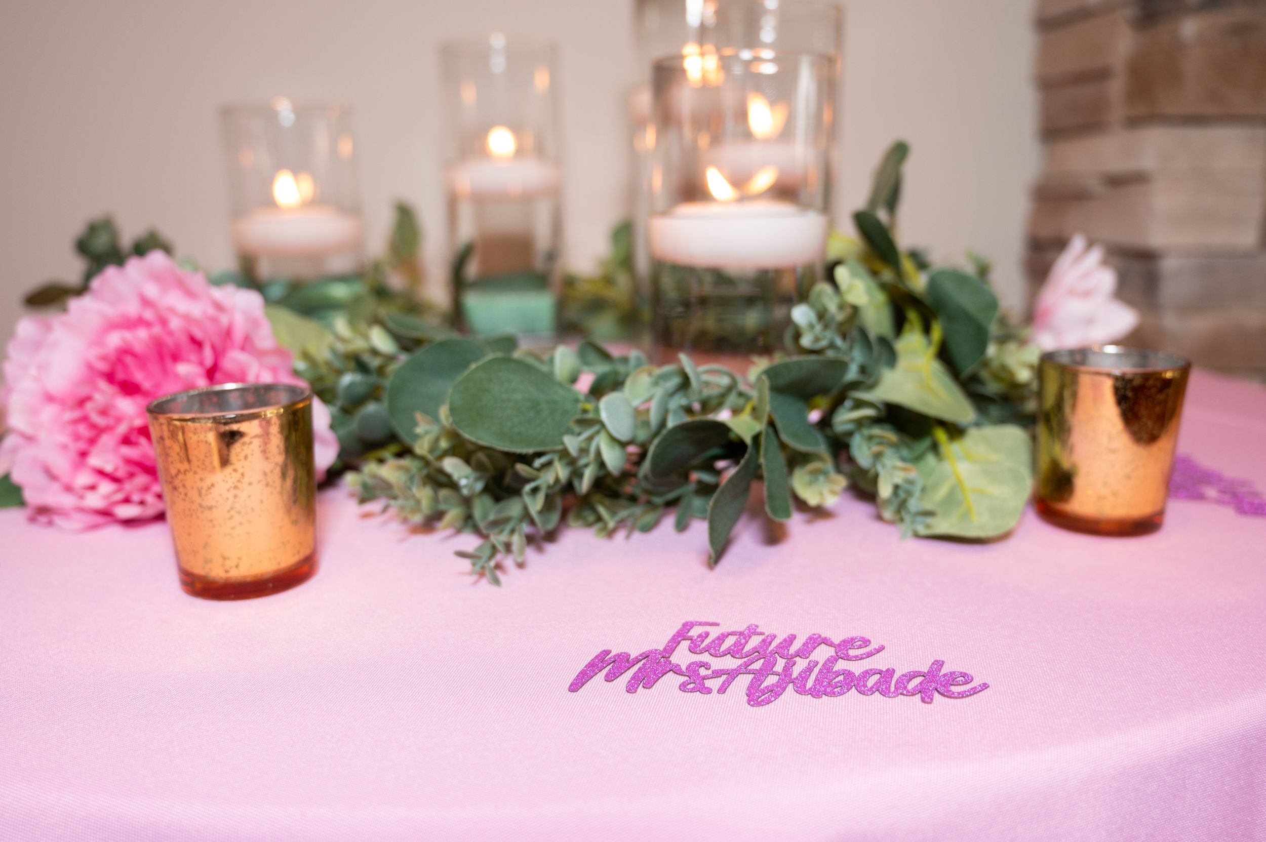 Pink and white wedding reception table with candles, flowers and greenery decorations on a tablecloth.