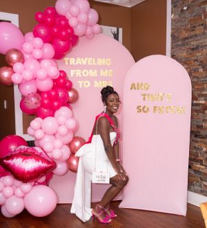Pink balloon arch and decorative doorway setup for special event with gold lettering.