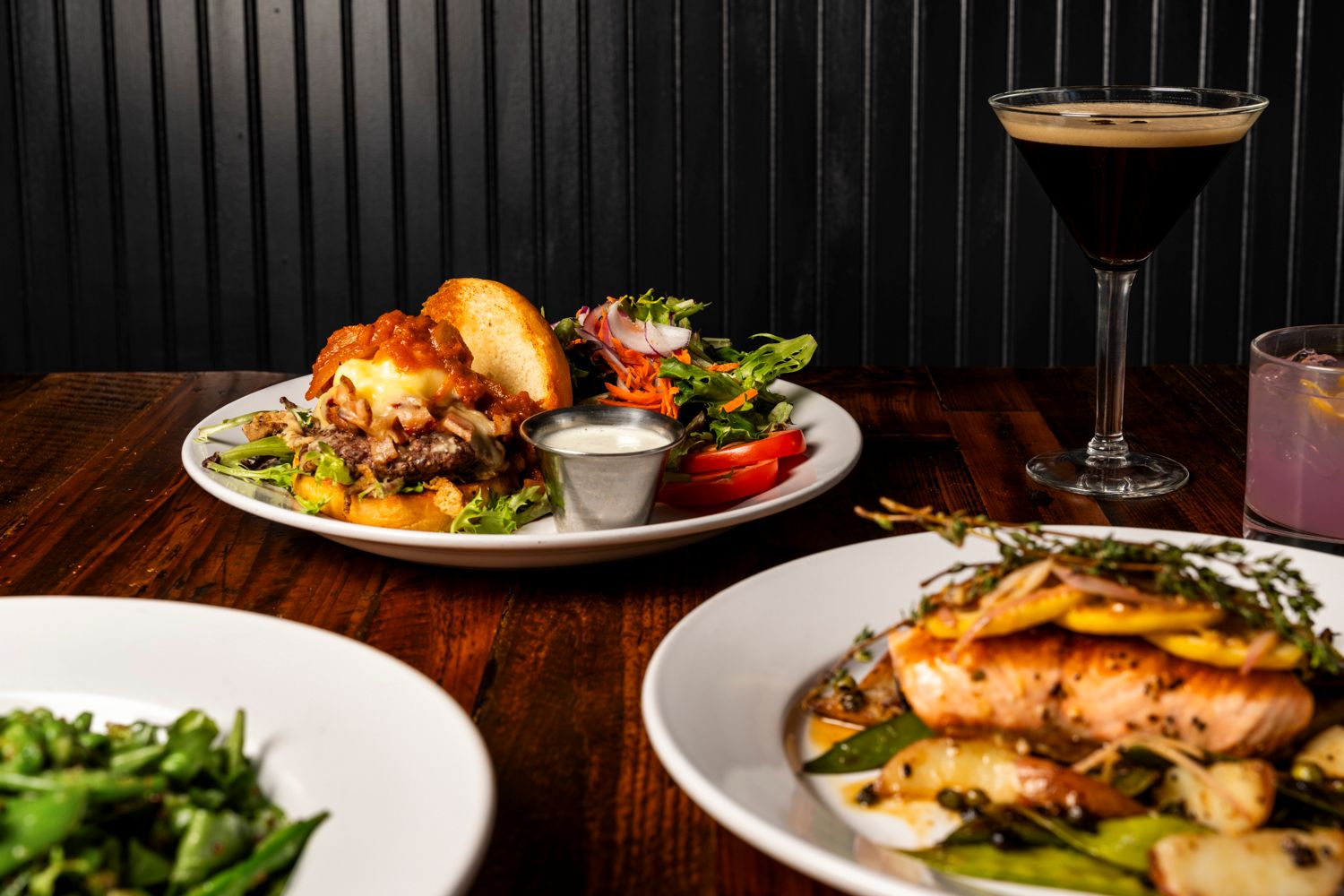 Elegant plated dinner with grilled salmon and salad alongside a cocktail on a dark wooden table.