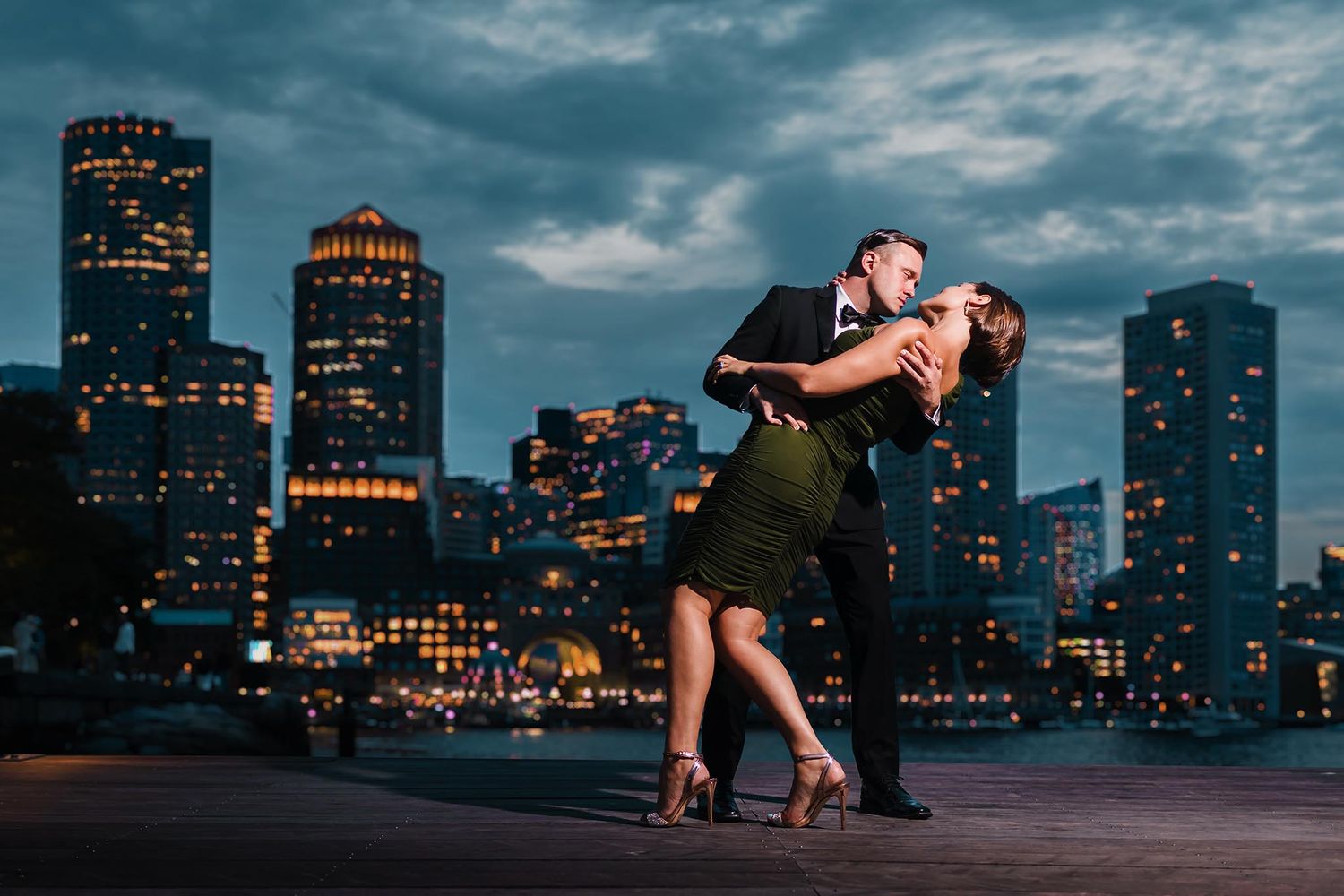 The groom to be dips his bride for a dramatic pose during their engagement session at dusk over looking Boston Harbor
