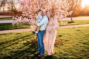 A family poses together in front of blooming cherry blossom trees at sunset.