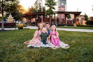 A family sits together on a blanket in a park during golden hour with a clock tower visible.