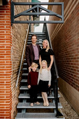 A family poses together on modern metal stairs between brick walls in an outdoor architectural setting.