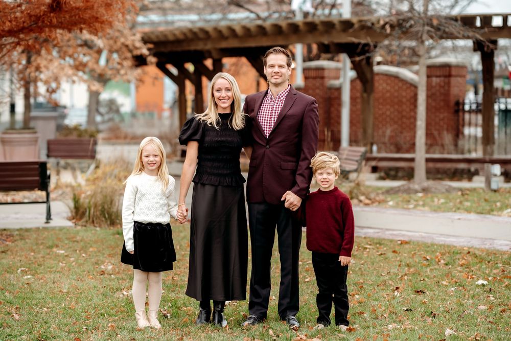 A group of people standing together outdoors in autumn, wearing coordinated burgundy and black outfits for a photo.