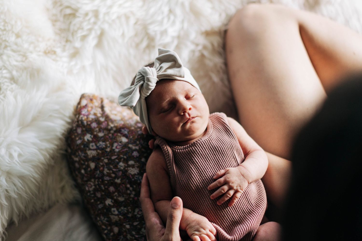 Newborn baby in pink knit outfit resting peacefully on white fur blanket.