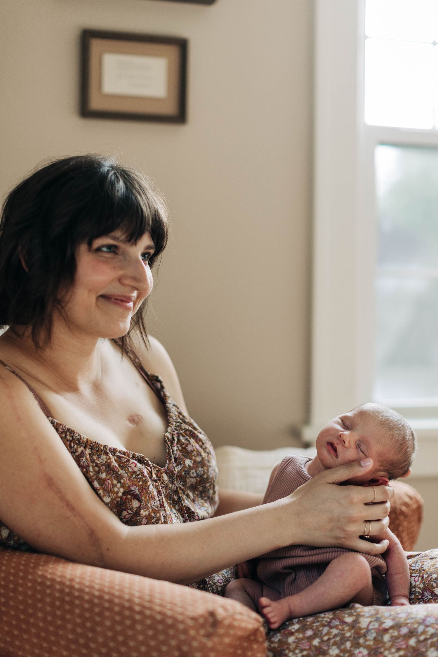 Sweet bonding moment between parent and newborn in comfortable armchair by window.