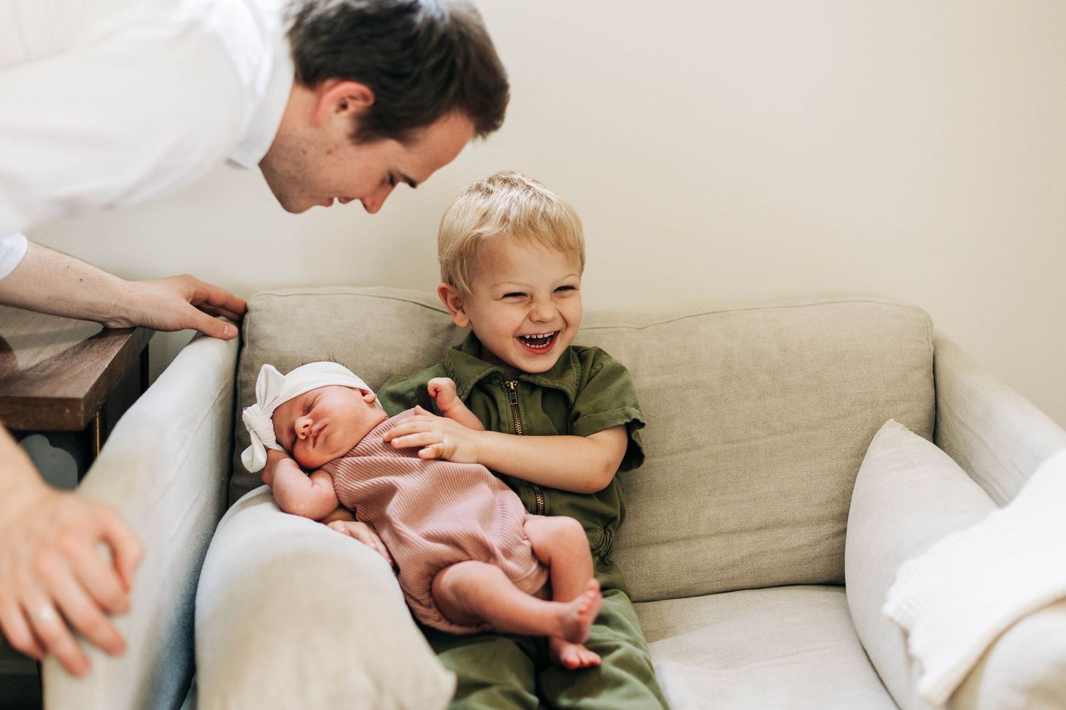 Joyful moment shared on couch while admiring newborn in pink outfit.