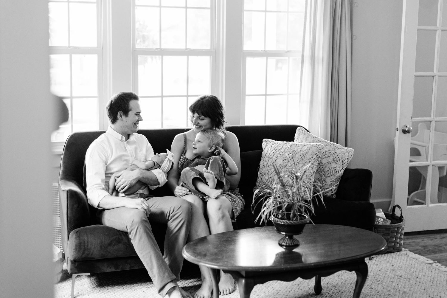 Black and white photo of couple seated on dark couch with decorative plant centerpiece.