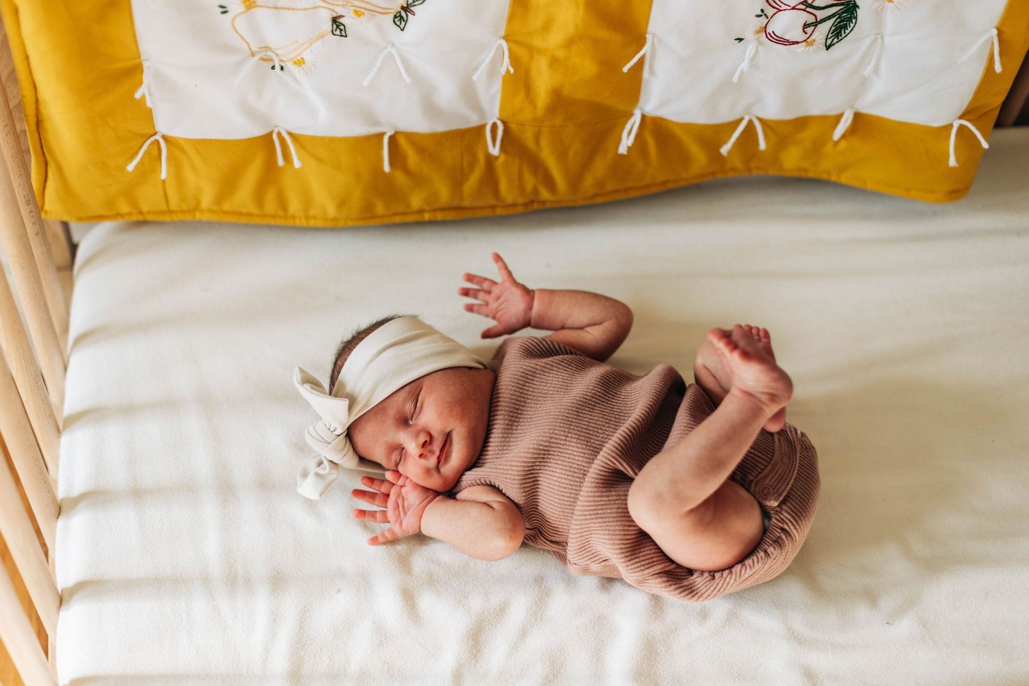 Sleeping newborn in pink outfit rests on white and yellow crib bedding.